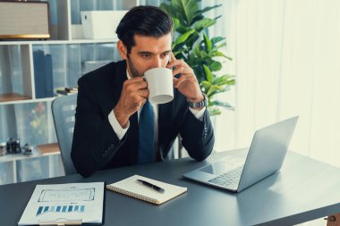 Modern ofis çalışma alanında çalışan bir işadamı elinde bir fincan kahveyle telefon görüşmelerini cevaplarken ya da çalışanları yönetirken. Coşkulu