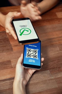 QR kodu parasız ödeme taraması için ekranda gösterilir. Kapalı eller, mobil uygulamadan elektronik işlem yoluyla para aktarmak için akıllı telefonu tutuyor. Hızlı ödeme için barkod teknolojisi. Coşkulu.