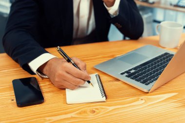 Modern ofis masasındaki modern profesyonel iş adamı çalışmak ve notlar yazmak için dizüstü bilgisayar kullanıyor. Ofisinde bilgisayar defteri üzerinde çalışan çalışkan bir ofis çalışanı. coşkulu