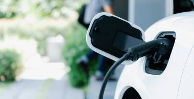 Focus electric car charging at home charging station with blurred progressive man walking in the background. Electric car using renewable clean for eco-friendly concept.