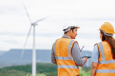 Erkek ve kadın mühendisler kırsal kesimdeki bir tepenin tepesinde ya da dağda rüzgar çiftliğinde çalışıyorlar. Yenilenebilir ve sürdürülebilir enerjinin gelecekteki üretimi için yenilikçi idealler.