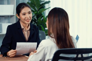 İki Asyalı kadın ofiste iş görüşmesi yapıyor. Başvuranlar özgeçmişi ve iş başvurusu hakkında konuşurken resmi takım giyerler. Muhabir olumlu ve konuşkan bir şekilde sorgulama talep ediyor. Coşkulu.