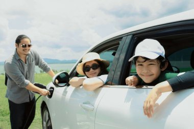 Concept of progressive happy family enjoying their time at green field and lake with electric vehicle. Electric vehicle driven by clean renewable from eco-friendly power sauce.