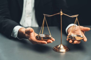 Siyah takım elbiseli bir avukat, altın bir denge, hukuki adalet ve dürüstlük sembolü, mahkemede dengeli ve etik karar verme mekanizması ile birlikte bürosunun masasında dikkatle oturuyor. denge