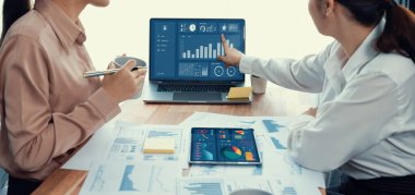 Analist ekip arkadaşı dijital gösterge panelinde finansal verileri tartışır, grafikleri dizüstü bilgisayar ve tablet ekranda analiz eder. Modern ofis pazarlama planlamak için iş zekasını kullanır. Coşkulu.