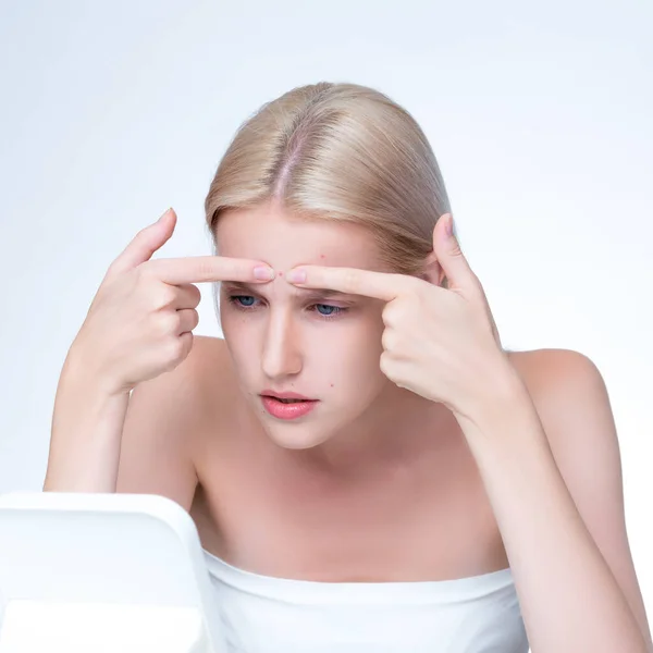 Acne problem troubling personable worried woman with natural beauty skin checking her face squeezing pimple spots in isolated background. Copyspace for blemish skincare treatment problem.