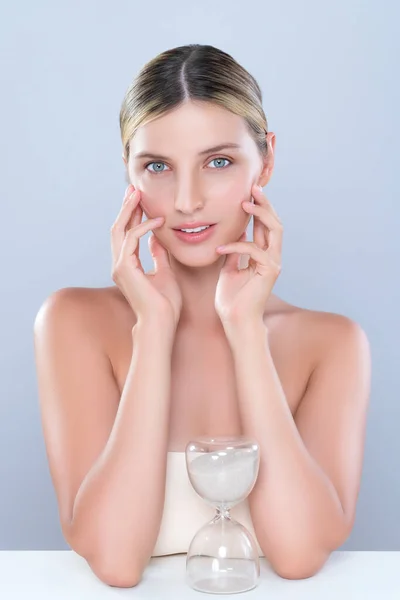 Alluring beauty model using hourglass in beauty concept of anti-aging skincare treatment for woman. Beautiful caucasian women portrait with perfect smooth clean skin in isolated background.