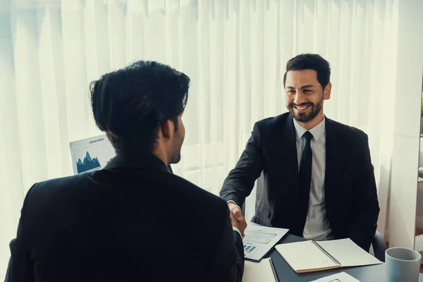 Business partnership meeting with successful trade agreement with handshake or greeting in corporate office desk. Businessman in black suit shaking hand after finalized business deal. Fervent