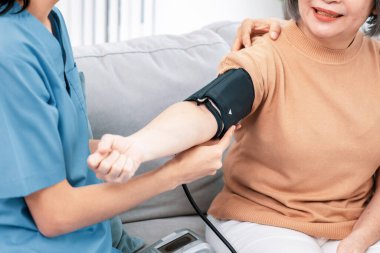 An elderly woman with a contented life having a blood pressure check by her caregiver at home with a smiley face.
