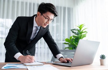 Ofis masasında dizüstü bilgisayarda çalışan bir iş adamı. Akıllı yönetici finansal iş verilerini araştırıyor ya da bilgisayarla stratejik iş pazarlaması planlıyor. Sevinçli.