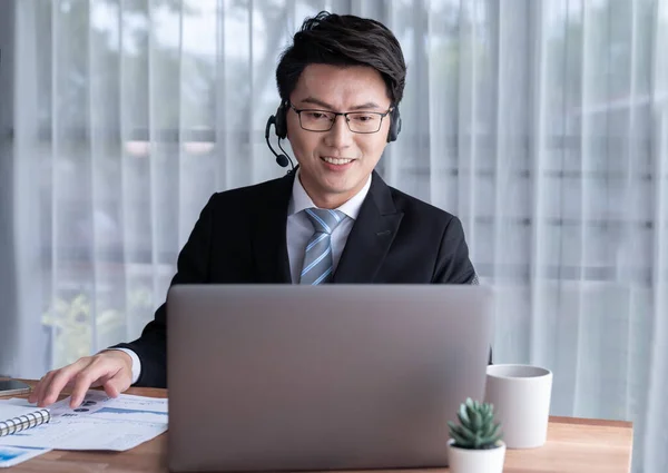 stock image Confident asian telesales businessman work in modern office wearing headphone, presenting BI dashboard analysis to clients and customers in online meeting. Success modern telesales business . Jubilant