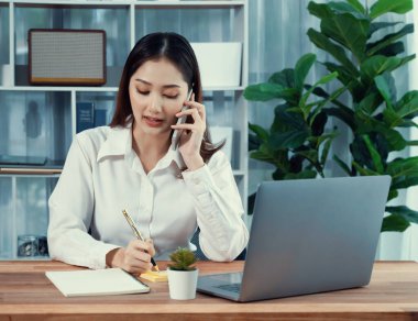 Genç hevesli iş kadını iş görüşmesinde konuşuyor ve laptopuna çoklu ofis hanımı olarak notlar yazıyor. Müşterilerle telefonda konuşurken iş ödevleri yazan kadın çalışan.