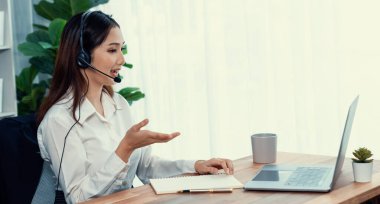 Bilgisayarında mikrofon ve kulaklıkla Asyalı çağrı merkezi çalışıyor. Kadın operatör istisnai müşteri hizmetleri sunar. Destek veren çağrı merkezi ajanı, müşteriye soruşturmada yardım ediyor. Coşkulu.