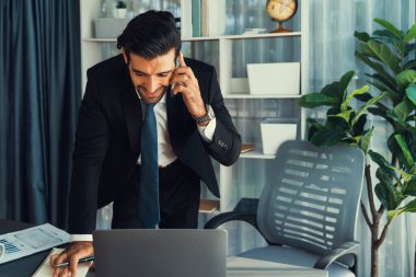 Çalışkan işadamı, ofisindeki dizüstü bilgisayarla cep telefonlu, modern, çalışkan ofis çalışanı yaşam biçimi konsepti olarak çalışırken müşterileriyle telefonda konuşmakla meşgul. Coşkulu