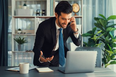 Çalışkan işadamı, ofisindeki dizüstü bilgisayarla cep telefonlu, modern, çalışkan ofis çalışanı yaşam biçimi konsepti olarak çalışırken müşterileriyle telefonda konuşmakla meşgul. Coşkulu