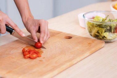Close up hands holding a knife preparing a contented meal. Sliced tomatoes and other vegetables on the glass dish.
