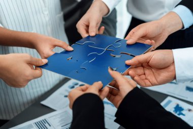 Closeup top view business team of office worker putting jigsaw puzzle together over table filled with financial report paper in workplace with manager to promote harmony concept in meeting room.