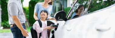 Progressive young happy family with electric vehicle and home backyard charging station. Green and clean energy from electric vehicles for healthy environment. Eco power from renewable source.