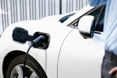 Arka planda bulanık bir işadamıyla şehrin kamu şarj istasyonundaki şarj bataryasına odaklan. Çevre dostu fikir için elektrikli şarjlı EV araba.