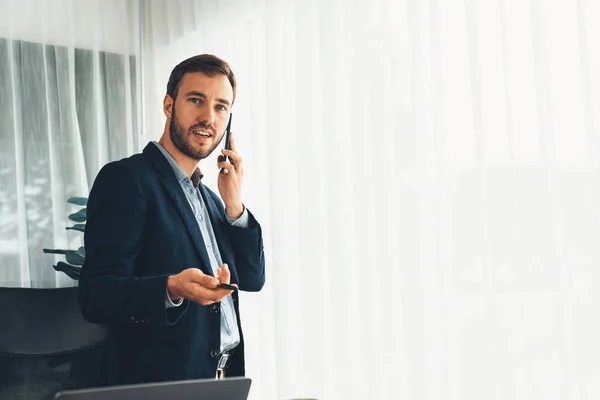 stock image Hardworking businessman stand confidently in modern office making persuasive sales call to client. Office worker talking on the phone coordinate and manage business work with colleagues. Entity