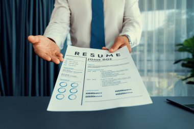 Resmi ofiste takım elbise giyen kendine güvenen bir adam, iş görüşmesi sırasında özgeçmiş kağıtlarını tutuyor. Röportajcı bakış açısına göre aday, özgeçmiş ödevini kamera önünde değerlendirmek üzere sunuyor. Coşkulu