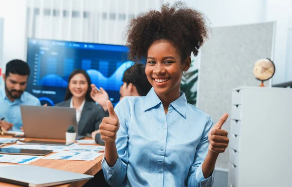 Bir grup ofis çalışanı ile birlikte arka planda ekranda gösterim paneliyle buluşan mutlu Afrikalı genç bir iş kadını portresi. Takım toplantısında kendine güveni tam bir ofis hanımı. Uyum