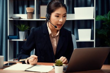 Bilgisayarında mikrofon ve kulaklıkla Asyalı çağrı merkezi çalışıyor. Kadın operatör istisnai müşteri hizmetleri sunar. Destek veren çağrı merkezi ajanı, müşteriye soruşturmada yardım ediyor. Coşkulu.