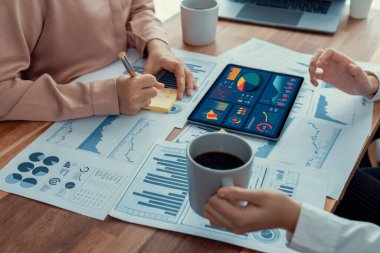 Analist ekip arkadaşı dijital gösterge panelinde finansal verileri tartışır, grafikleri dizüstü bilgisayar ve tablet ekranda analiz eder. Modern ofis pazarlama planlamak için iş zekasını kullanır. Coşkulu.