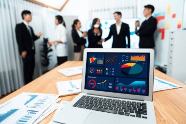 Focus laptop monitor display dashboard report by business intelligence, analyzed financial data for planning market strategy with blur background of standing office worker discussing in harmony office