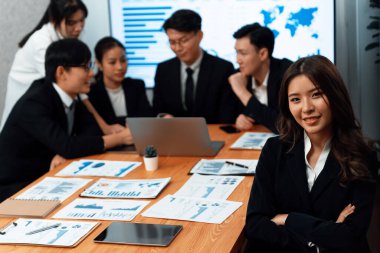 Focus portrait of female manger, businesswoman in the harmony meeting room with blurred of colleagues working together, analyzing financial paper report and dashboard data on screen in background.