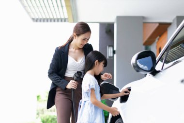 Evde şarj edilen elektrikli bir araçla okuldan yeni dönen anne ve kızın ilerici yaşam tarzı. Elektrikli araç, sürdürülebilir temiz enerjiyle çalışıyor..