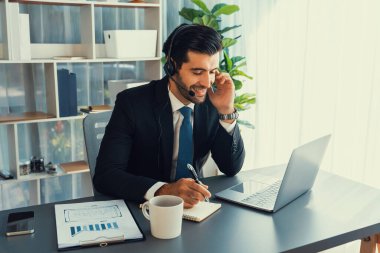 Erkek çağrı merkezi operatörü ya da telesales temsilcisi ofis masasında oturmuş kulaklık takıyor ve müşteri hizmetleri desteği sağlayan ya da satış yapan müşteriyle sohbet ediyor. coşkulu
