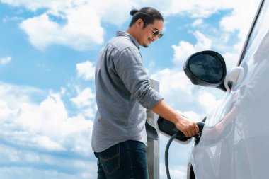 Elektrikli arabası ve bulutlu geçmişi olan ilerici bir adam. Temiz, yenilenebilir şarj noktası olan bir EV araba. Çevreyi yeşil enerjiden ferahlatıyor.