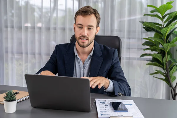 Businessman holds virtual office meeting from office desk, discussing with online video conference using webinar application on laptop for distant communication with remote workers. Entity