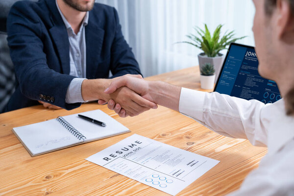 After successful meeting or job interview, two happy businessmen shake hands over resume papers. HR manager extend hand for congratulatory handshake to job applicant, welcoming new employee. Entity