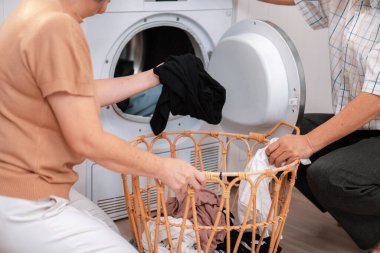 Senior couple working together to complete their household chores at the washing machine in a happy and contented manner. Husband and wife doing the usual tasks in the house.