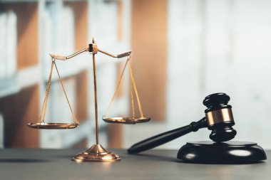 Adalet ve hukuki otorite kavramının simgesi olarak mahkeme kütüphanesinde parlak altın dengeli ölçek ve ahşap tokmak avukat ve yargıç tarafından eşitlik ve adil yargılamayı yansıtıyor. denge