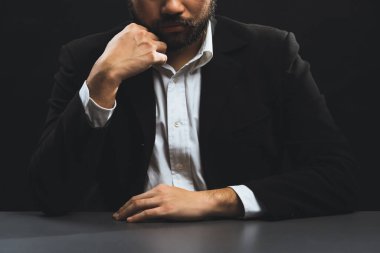 Resmi siyah takım elbiseli bir iş adamı ya da avukat izole edilmiş siyah arka planda oturuyor. Otorite ve ciddi jestleri olan bir adam kavramı. denge
