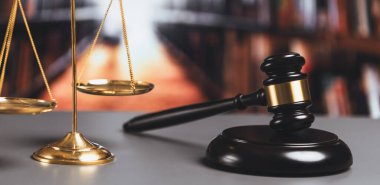 Adalet ve hukuki otorite kavramının simgesi olarak mahkeme kütüphanesinde parlak altın dengeli ölçek ve ahşap tokmak avukat ve yargıç tarafından eşitlik ve adil yargılamayı yansıtıyor. denge