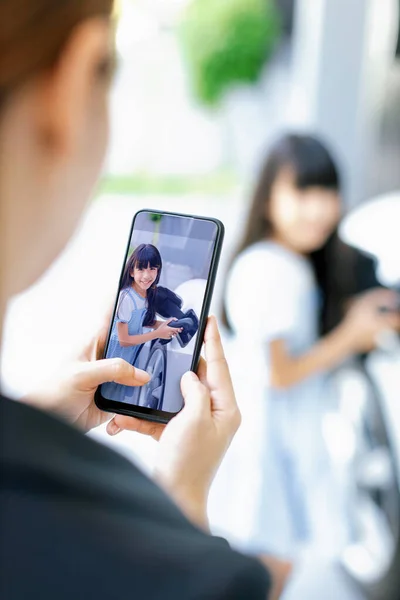 Stock image Progressive mother using smartphone take focus photo of daughter recharge EV car. Image of asian girl insert electric charger from home charging station to EV car on phone screen with blur background.