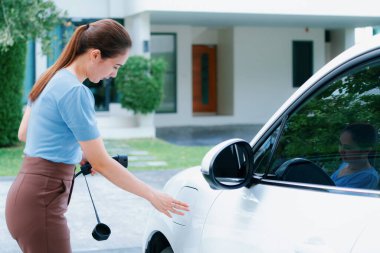 Progressive woman install cable plug to her electric car with home charging station. Concept of the use of electric vehicles in a progressive lifestyle contributes to clean environment.
