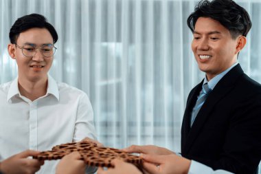 Closeup hand holding wooden gear by businesspeople wearing suit for harmony synergy in office workplace concept. Group of people hand making chain of gears into collective form for unity symbol.