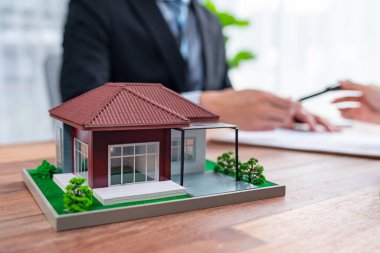 Emlakçı, alıcı ya da müşterinin bulanık geçmişine sahip ahşap masadaki ev modeli örneği ev kredisi sözleşmesindeki şartları ve koşulları tartışıyor. Konut işleri toplantısı. Sevinçli.