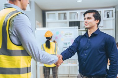 An engineer with a protective vest handshake with an investor in his office. Following a successful meeting, employee and employer form a partnership.