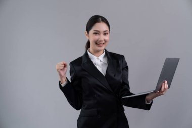 Kendine güvenen genç iş kadını izole edilmiş bir zeminde duruyor ve resmi siyah takım elbiseyle dizüstü bilgisayarda çalışıyor. Ofisteki kadın ya da yönetici, zeki ve profesyonel görünümlü. Coşkulu.