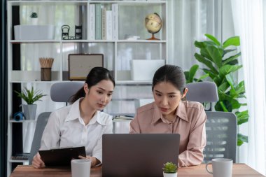 Modern ofis çalışma alanında iş birliği yapan iki genç ofis çalışanı, modern ofis çalışanı olarak profesyonelliklerini sergileyerek, dizüstü bilgisayarda tartışıyorlar ve birlikte çalışıyorlar. Coşkulu.