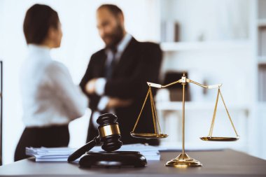 Adalet ve tokmak çekicinin dengeli ölçeğinde, avukat meslektaşlarının hukuki temsilciler olarak hukuk bürosunda görüşüp dava açmayı planladıkları bulanık arka planı üzerinde duruluyor. Eşitlik