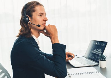 Erkek müşteri hizmetleri operatörü ya da telesales temsilcisi ofiste oturuyor, kulaklık takıyor ve müşteriyle satış desteği ya da kapanış konuşması yapıyor. Çağrı merkezi portresi. Varlık