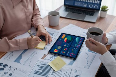 Analist ekip arkadaşı dijital gösterge panelinde finansal verileri tartışır, grafikleri dizüstü bilgisayar ve tablet ekranda analiz eder. Modern ofis pazarlama planlamak için iş zekasını kullanır. Coşkulu.