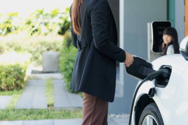 Evde şarj edilen elektrikli bir araçla okuldan yeni dönen anne ve kızın ilerici yaşam tarzı. Elektrikli araç, sürdürülebilir temiz enerjiyle çalışıyor..